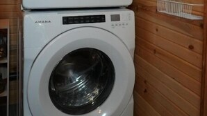 Kaksi päällekkäin asetettua, edestä täytettävää pesukonetta puisessa huoneessa, jossa on hyllyjä, joilla säilytetään puhdistusaineita.