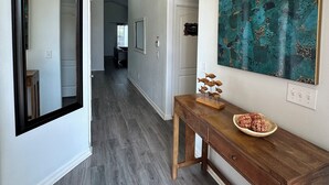 Um corredor com um aparador de madeira, um quadro abstrato azul-esverdeado e um espelho na parede.