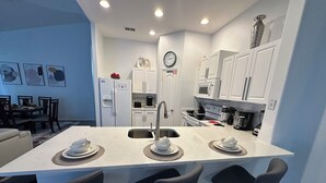 Uma cozinha moderna com armários brancos, uma ilha central com banquetas, uma pia e um relógio na parede.