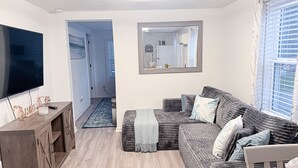 En moderne stue med et fladskærms-TV, træskabe, en grå sofa og et spejl på væggen.