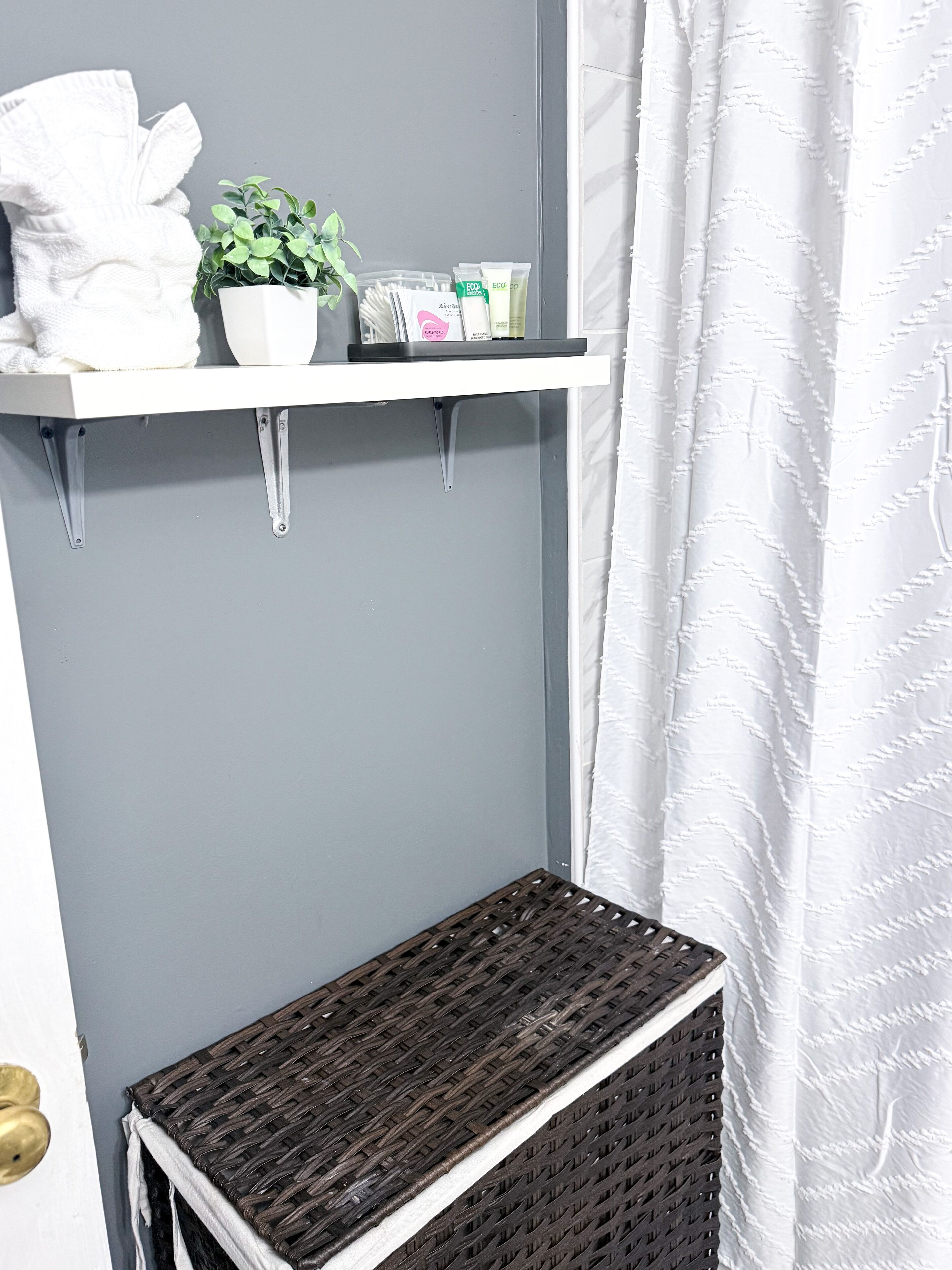 A bathroom with a white towel, a potted plant, and toiletries on a white shelf.