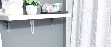 A bathroom with a white towel, a potted plant, and toiletries on a white shelf.