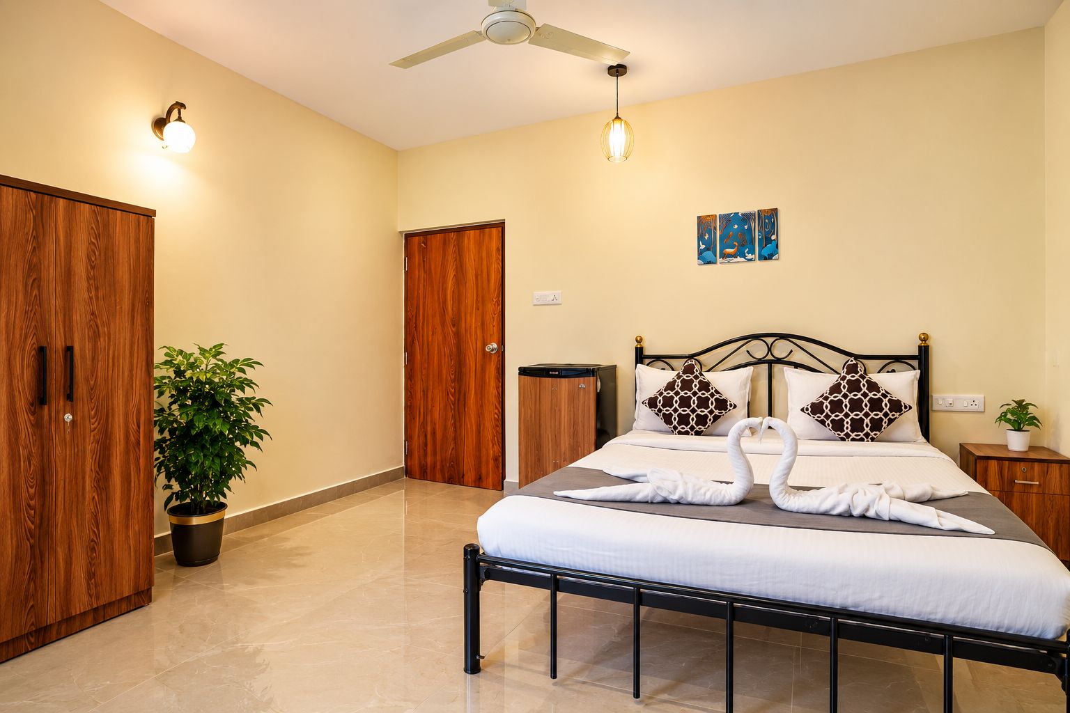 Une chambre d’hôtel avec un lit, un ventilateur de plafond, une plante en pot et un luminaire fixé au mur.