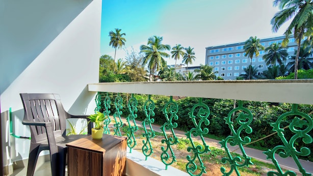 A balcony with a wooden table, a plastic chair, and a potted plant. - The Coral Reef (Candolim)