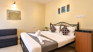 A hotel room with a bed, a sofa, a bedside table with a plant, and a small cabinet.