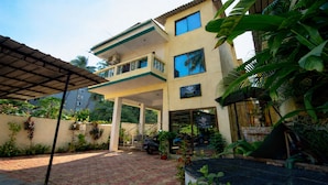 A two-story building with a covered patio area, a staircase, and a view of the surrounding greenery. - The Coral Reef (Candolim)