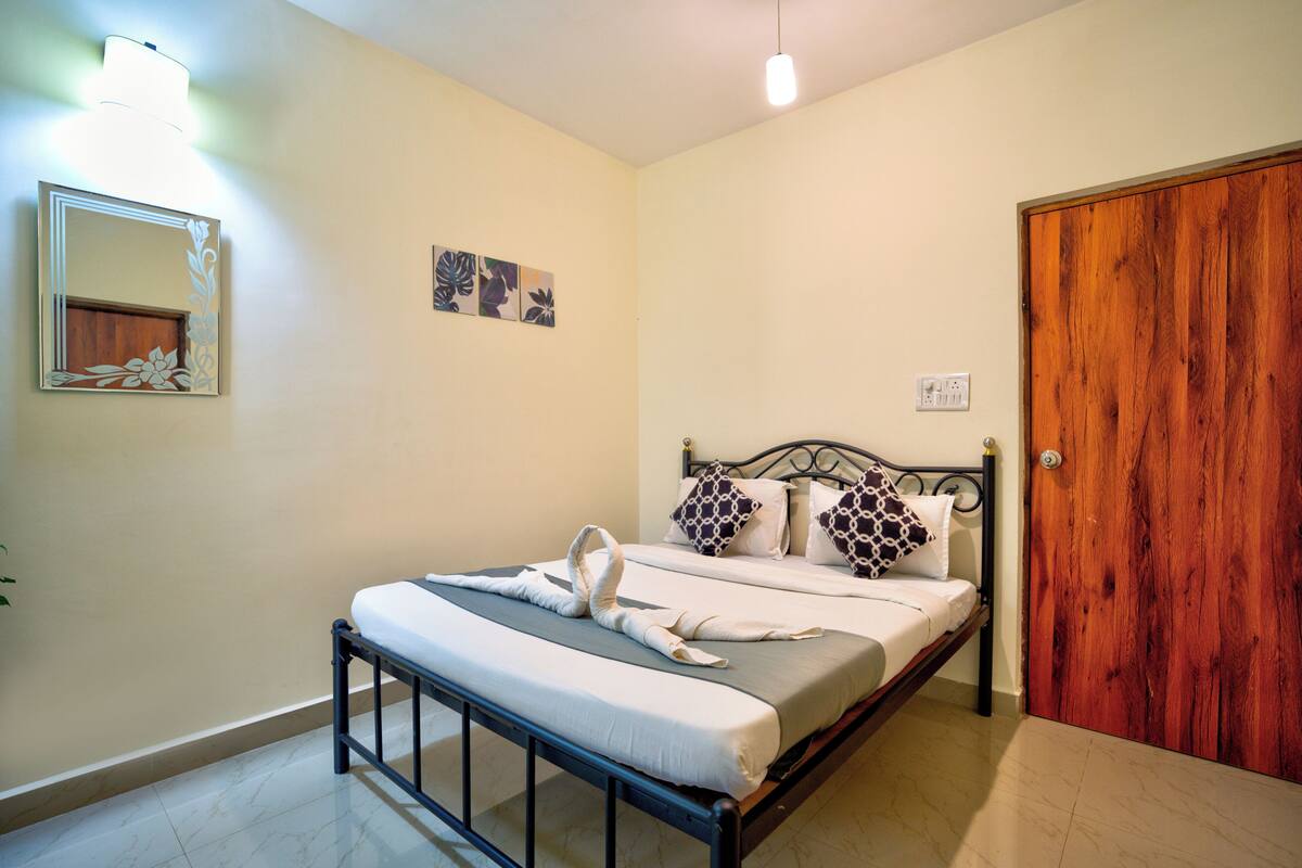 A neatly made bed with a towel, a wooden door, and a wall-mounted light fixture.