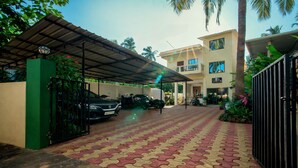 A covered parking area with a patterned pavement leading to a building with multiple windows and a balcony. - The Coral Reef (Candolim)