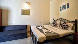 A neatly made bed with a blanket and pillows, a bedside table with a plant, and a wall-mounted mirror. - The Coral Reef (Candolim)