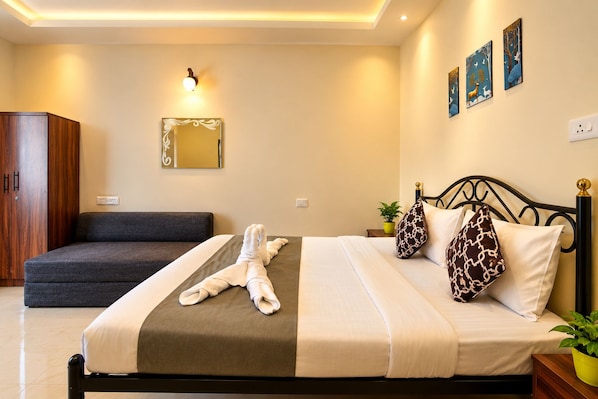 A hotel room with a bed, a sofa, a mirror, wall art, and a potted plant. - The Coral Reef (Candolim)