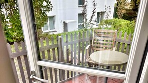 Une porte-fenêtre coulissante donne sur un patio extérieur agrémenté d’une table et de chaises en bois, d’une clôture blanche et d’un sol en briques.