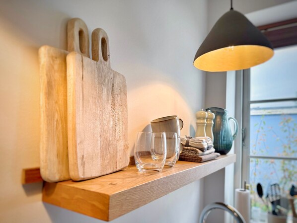 A wooden shelf with a rustic cutting board, a glass pitcher, and a glass set.