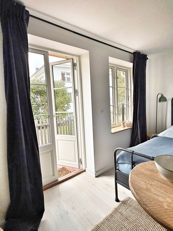 A bedroom with a bed, a small table, a window, and a door leading to a balcony. - Romantic apartment for 2 people - 200m to the Strelasund with a view of Stralsund (Altefähr)