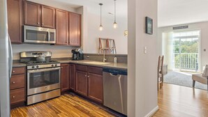 A modern kitchen with stainless steel appliances, wooden cabinets, and pendant lighting. - Grande at Canal 14 For 6ppl (Rehoboth Beach)