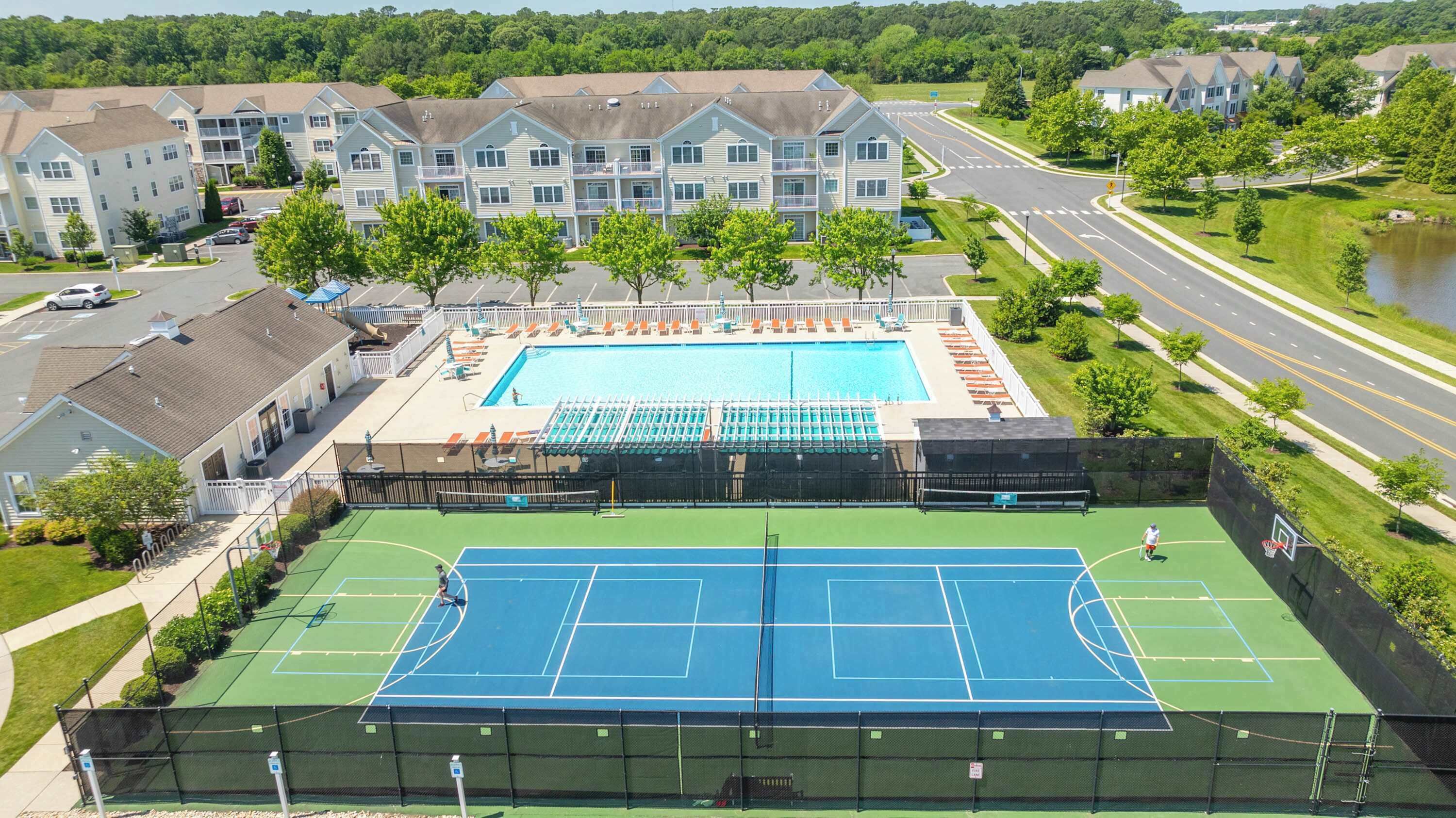 Un complejo residencial con piscina, canchas de tenis y una carretera con puente.