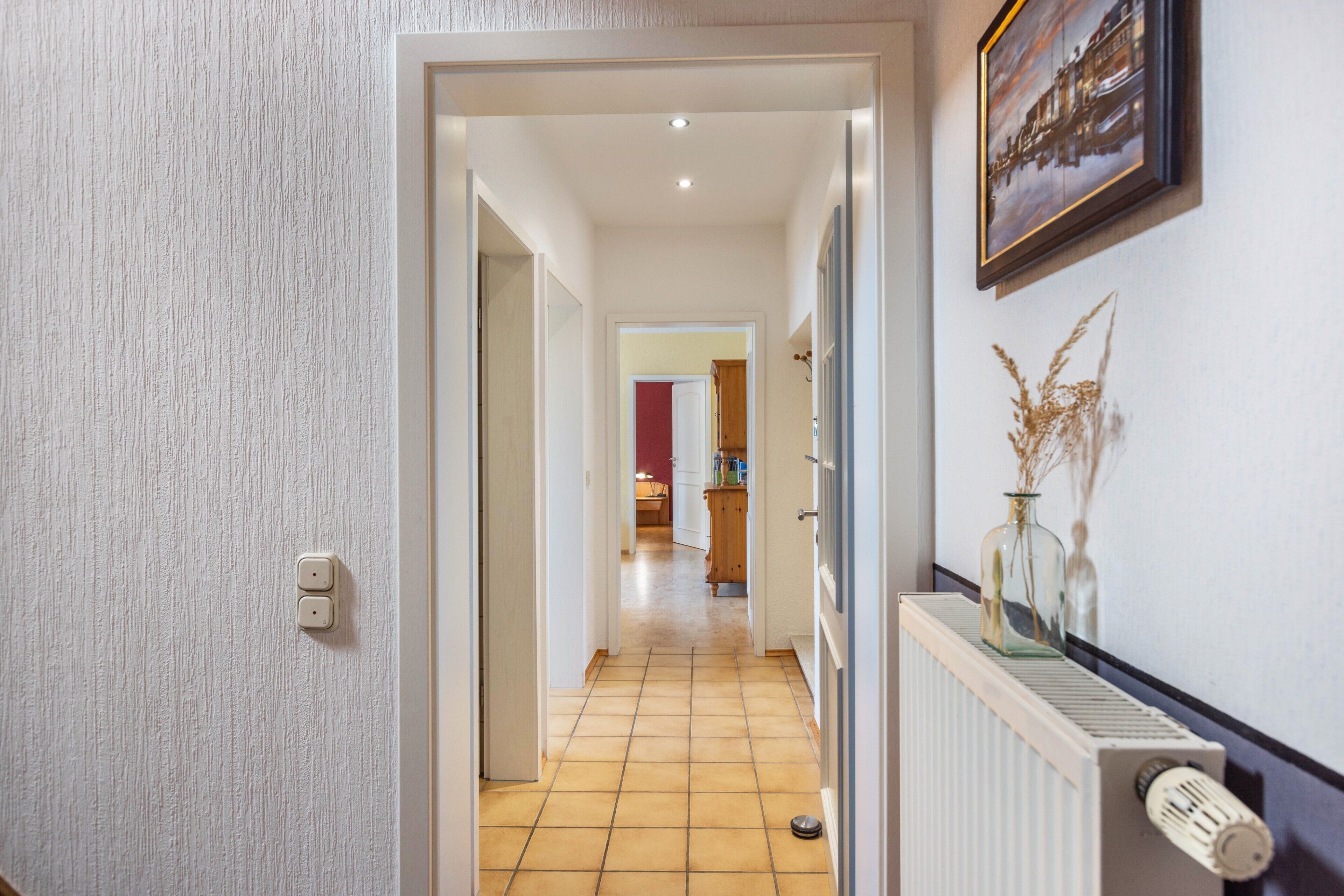 A hallway with a radiator, a door with a light switch, and a framed picture on the wall.