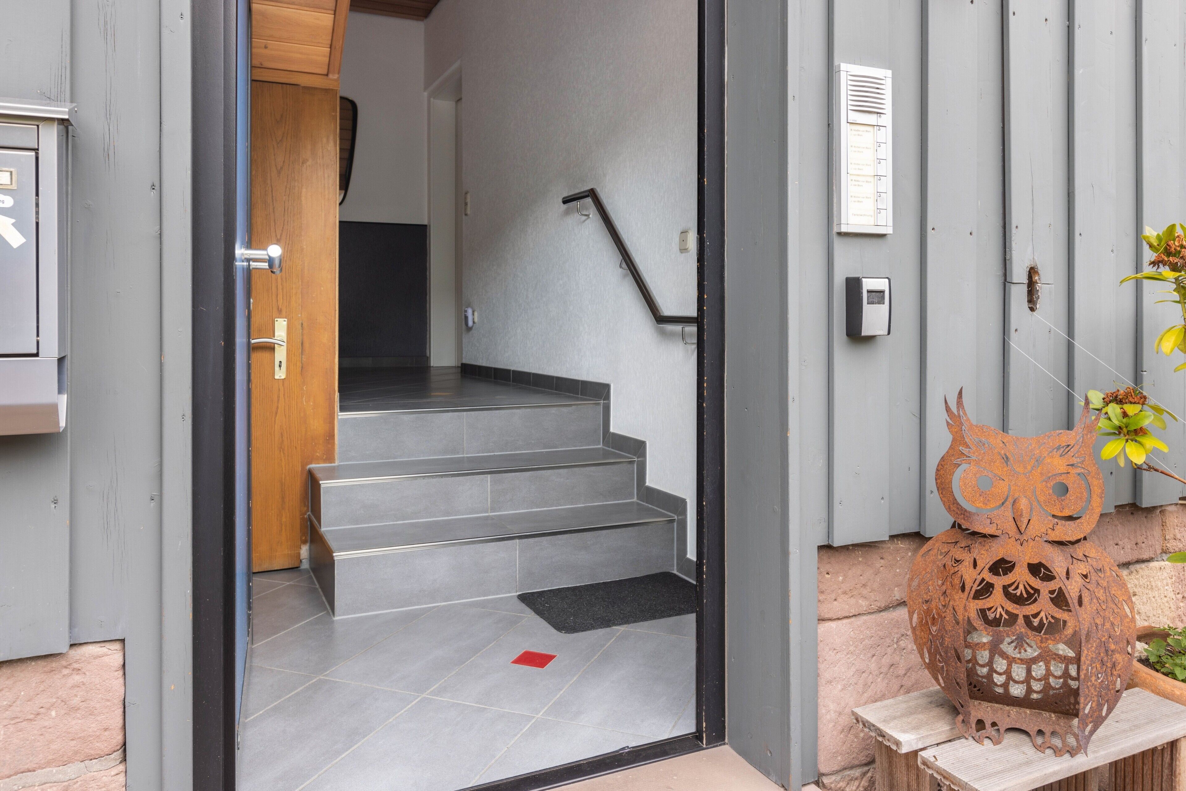 Une entrée moderne avec une porte en bois, un escalier en métal et une décoration en forme de hibou également en métal.
