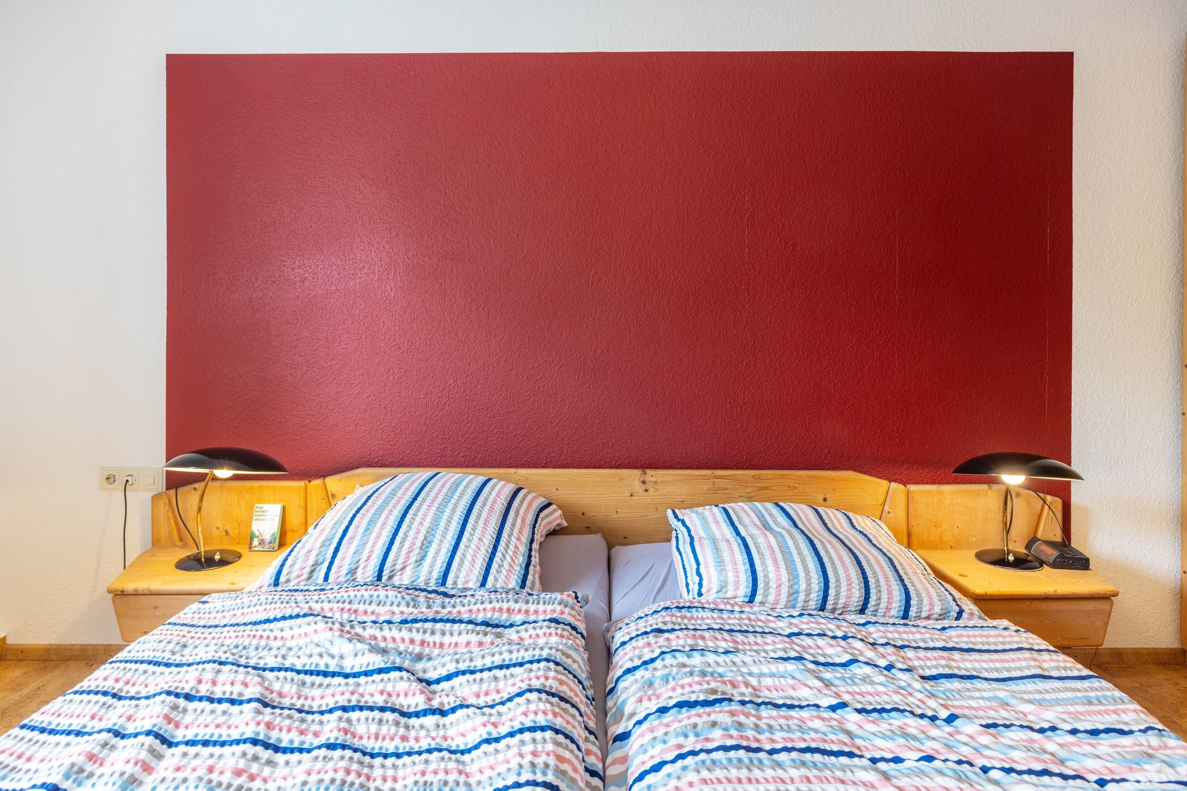 A double bed with striped bedding, two bedside tables with lamps, and a red headboard.