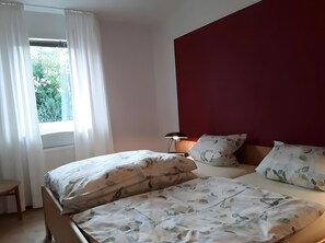 A bedroom with a bed, a nightstand, a lamp, and a window with curtains.