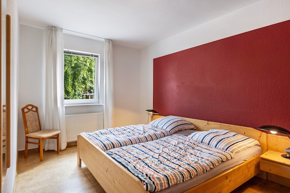 A bedroom with a bed, a chair, a window with curtains, and a red wall.