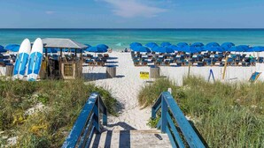 Ein Strand mit blauen Sonnenschirmen und Liegestühlen, einer Holzkonstruktion und einem Schild, das Zelte verbietet.