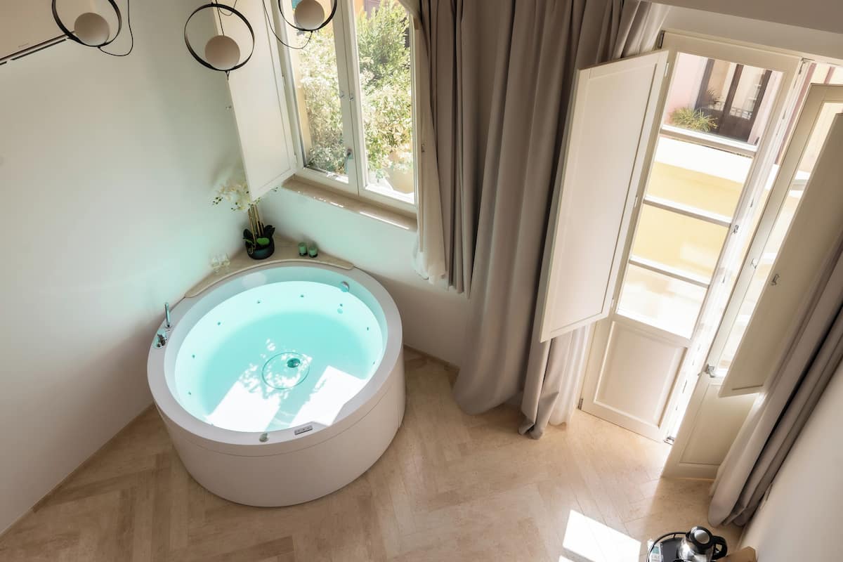 Une salle de bain dotée d’une grande baignoire, d’une fenêtre avec des rideaux et donnant sur le balcon extérieur.
