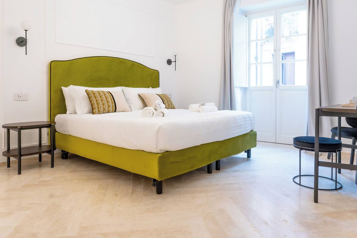 Un lit bien fait, avec une tête de lit verte, une table de chevet et une chaise.