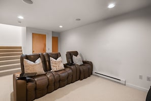 Une salle de cinéma maison avec un canapé inclinable en cuir marron, un ordinateur portable et un radiateur fixé au mur.