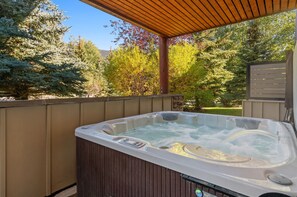 A hot tub under a wooden pergola with a view of trees and a stone wall.