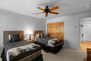 A bedroom with two beds, a ceiling fan, a nightstand with a lamp, and a wooden wardrobe.