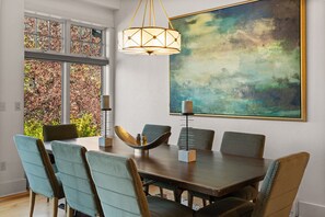 A dining room with a large table, six chairs, a chandelier, and a large abstract painting on the wall.