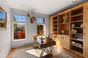 Une pièce avec un bureau en bois, des étagères et une grande fenêtre donnant sur une terrasse.