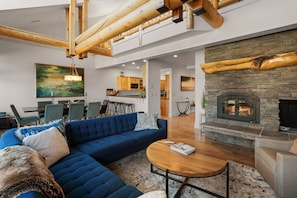 Un salon moderne avec un canapé d’angle bleu, une table basse ronde en bois et une cheminée en pierre.