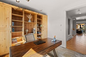 A home office with a wooden desk, open shelving, and a laptop.