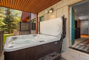 Un bain à remous sur une terrasse en bois, avec vue sur une maison et des arbres.