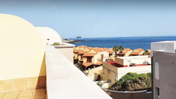 Ein Küstenwohngebiet mit Reihenhäusern, freiem Blick auf das Meer und einem Schiffen im entfernten Hintergrund.