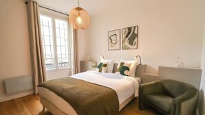 A bedroom with a large bed, a chair, a hanging light fixture, and two abstract paintings on the wall.