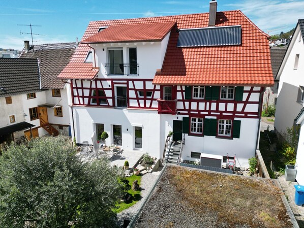 A two-story house with a red tiled roof, white walls, and a balcony.