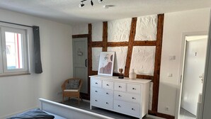 Een slaapkamer met een bed, een dressoir, een stoel en een deur.