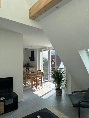 A modern interior with a dining area, kitchen, and a living space with a TV and seating.