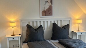 A bedroom with a white bed, two nightstands, a lamp on each, and a painting above the bed. - Apartment 'Ferienwohnung Seescheune' with Lake View and Wi-Fi (Bodman-Ludwigshafen)