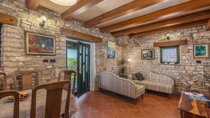 A rustic interior with stone walls, wooden beams, a dining area with chairs and a table, and a striped sofa.