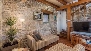 A cozy living room with a stone wall, a striped sofa, a television, and a staircase leading to another level.