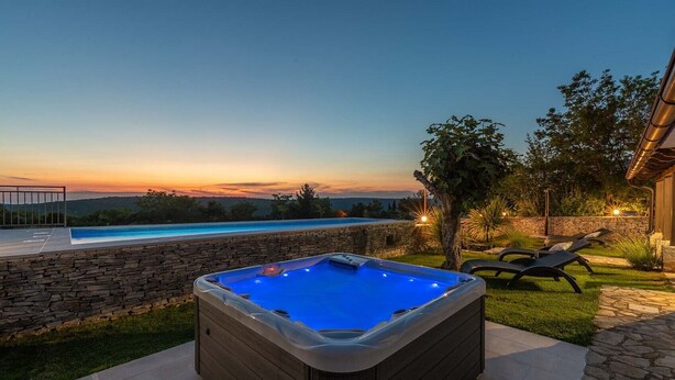 A hot tub in a backyard with a pool and stone walls.