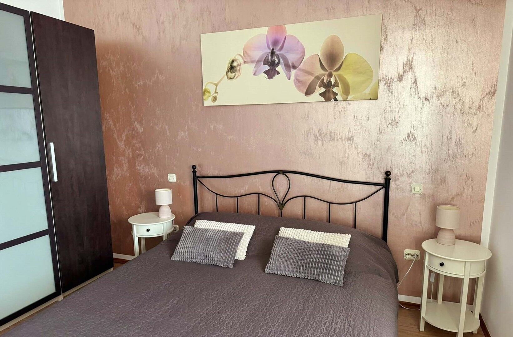 Quarto com cama, duas mesas de cabeceira, um quadro na parede e uma porta.