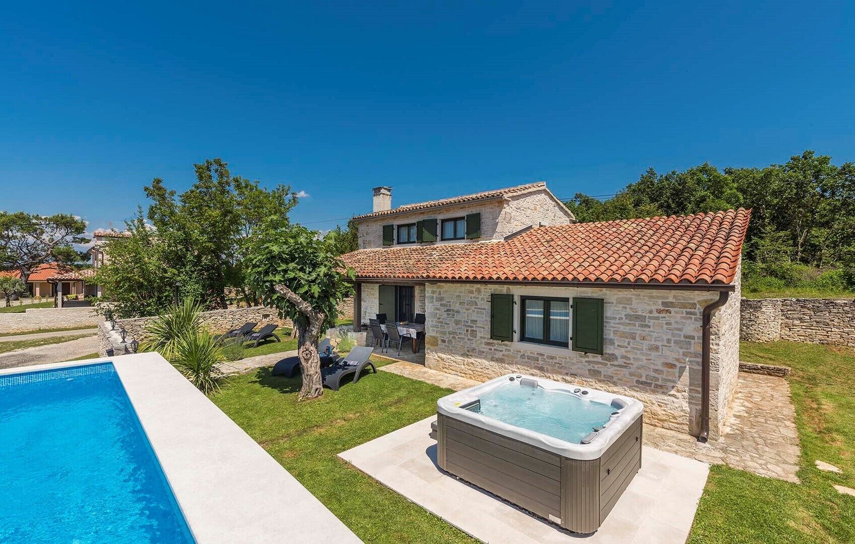 Une maison en pierre avec un toit en tuiles, une piscine et un jacuzzi.