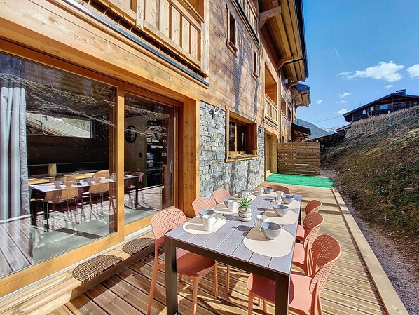 A wooden deck with tables and chairs, a stone wall, and a view of the mountains.