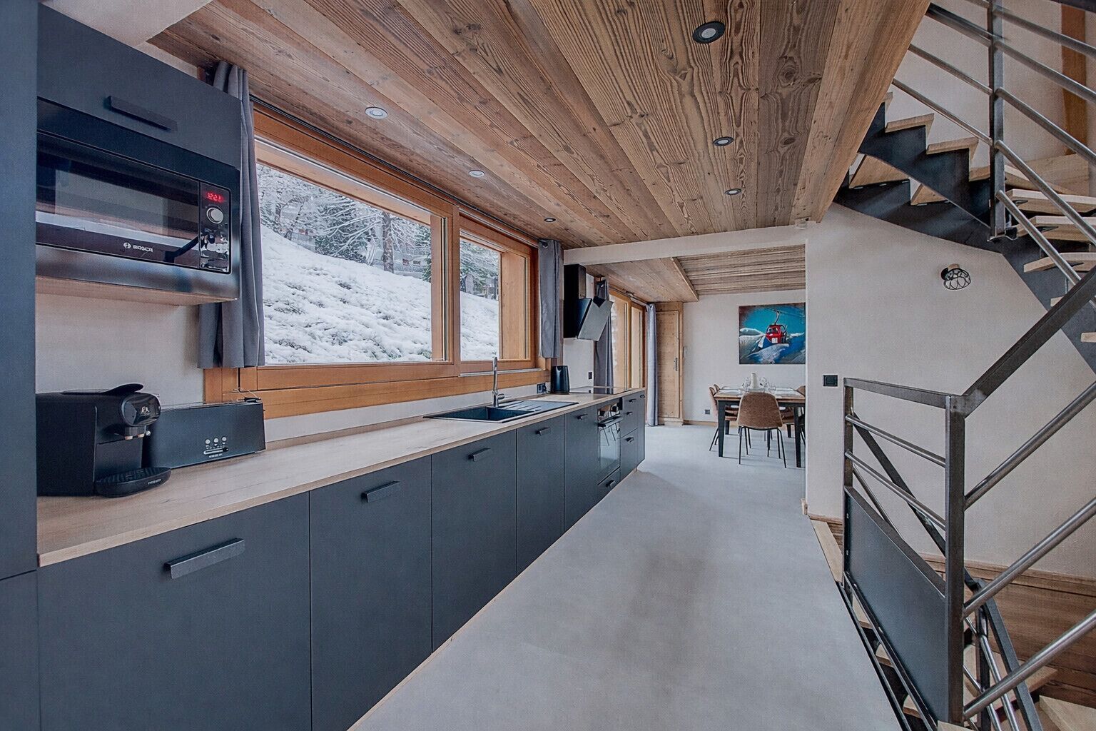 Una cocina moderna con una cafetera Bosch, un ventanal con vistas nevadas y una escalera.