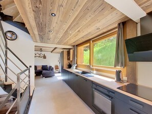 A modern kitchen with a large window, built-in appliances, and a wooden ceiling.