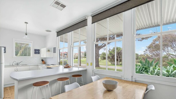 A modern kitchen with a large island, bar stools, and a dining table with a bowl. - 5 Rosetta Place, Hayborough (Hayborough)